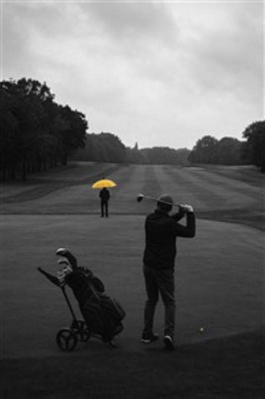 Golf i Regnvejr med Farverig Paraply - Oplev det perfekte møde mellem natur og sport med dette kunstværk, hvor golfspillere navigerer under en grå himmel, mens en strålende gul paraply lyser op i landskabet. Dette billede fanger både udfordringen ved golf og skønheden i regnvandets stilhed.